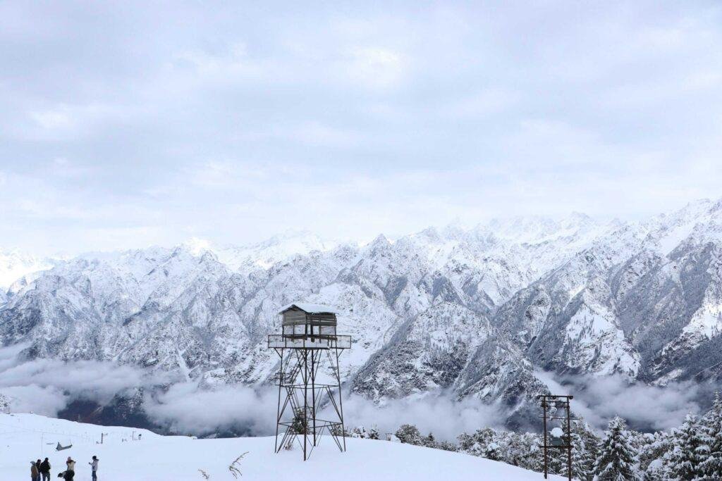 Snowy Himalayan mountains in Uttarakhand, India, with a watchtower and tourists enjoying the scenic views.